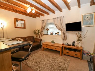 A living room with a brown leather sofa a wooden coffee table a television mounted on the wall and wooden ceiling beams at Bwthyn Ael Y Bryn in Criccieth