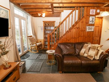 A living room with a brown leather sofa and a rocking chair near glass doors at Bwthyn Ael Y Bryn in Criccieth