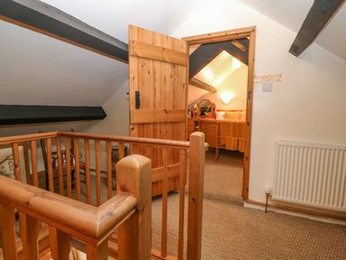 A hallway with wooden railing leading to a bedroom with a wooden door open at Bwthyn Ael Y Bryn in Criccieth