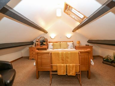 A bedroom with a wooden bed and nightstands under a sloped ceiling with skylight at Bwthyn Ael Y Bryn in Criccieth