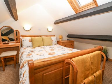 A bedroom with a wooden bed, two green cushions, a dressing table with a mirror, a nightstand with a lamp, and a skylight window at Bwthyn Ael Y Bryn in Criccieth