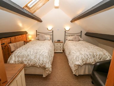 A bedroom with two single beds a small nightstand and a chair at Bwthyn Ael Y Bryn in Criccieth