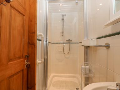 A shower area with glass door wooden door and wall-mounted shower at Bwthyn Ael Y Bryn in Criccieth