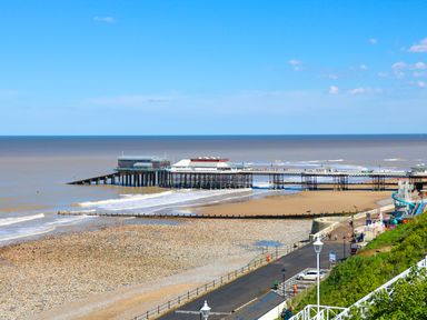 A beach with a pebble and sand shore and a pier extending over the water at Howards Hill West in Cromer