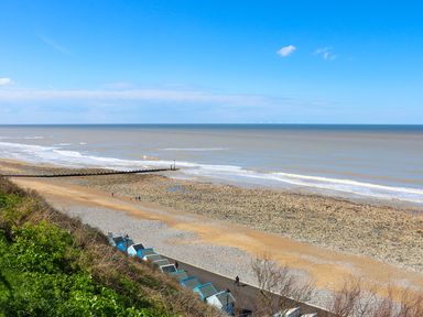 A rocky and sandy beach with small blue and gray beach huts along a path at Howards Hill West in Cromer