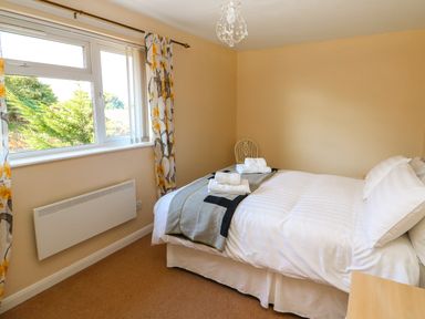 A bedroom with a bed with white linens and folded towels on it next to a window with floral curtains at Howards Hill West in Cromer