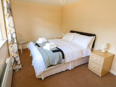 A bedroom with a double bed bedside tables lamps a chair and floral curtains at Howards Hill West in Cromer