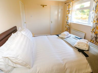 A bedroom with a made bed folded towels on top a window with floral curtains and a closed door at Howards Hill West in Cromer
