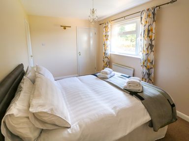 A bedroom with a bed made with white linens and rolled towels near a window with floral curtains at Howards Hill West in Cromer