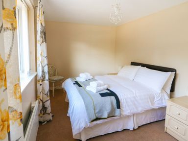 A bedroom with a double bed white linens folded towels floral curtains and a small chair at Howards Hill West in Cromer