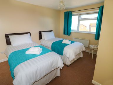A bedroom with two single beds with white bedding and teal runners next to a window with teal curtains at Howards Hill West in Cromer