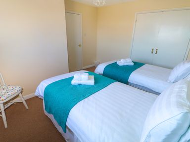 A bedroom with two single beds with white linens and turquoise runners at Howards Hill West in Cromer