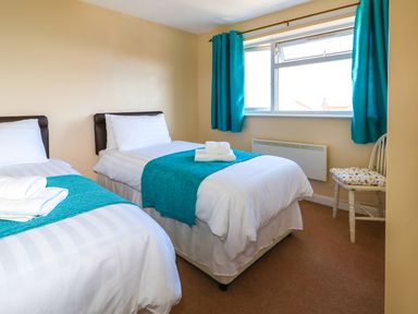 A bedroom with two single beds blue curtains and a wooden chair at Howards Hill West in Cromer