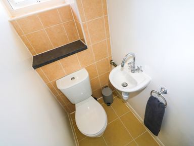 A small bathroom with a toilet a wall-mounted sink a towel ring with a dark towel and a waste bin at Howards Hill West in Cromer