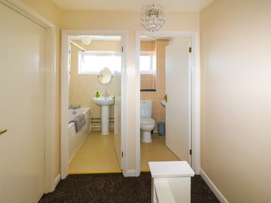 A hallway with two open doors showing a bathroom with a bathtub and sink and a separate toilet at Howards Hill West in Cromer