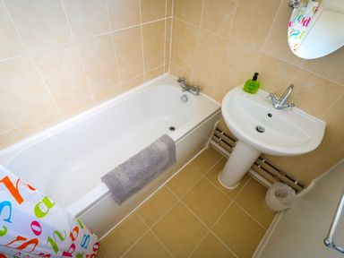 A bathroom with a bathtub a sink a soap dispenser and a colorful shower curtain at Howards Hill West in Cromer
