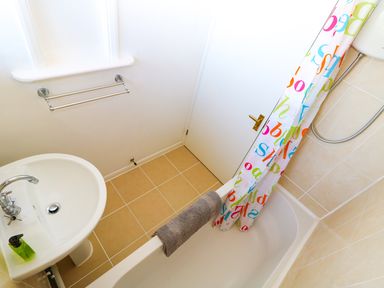 A bathroom with a white sink a towel rack a bathtub with a shower and a colorful shower curtain at Howards Hill West in Cromer