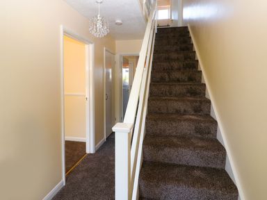A staircase with brown carpet leading up and a hallway with doors on the side at Howards Hill West in Cromer