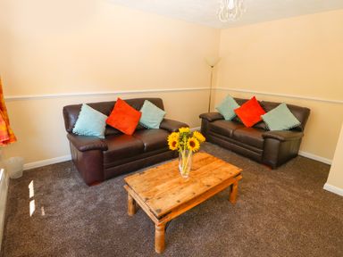 A living room with two brown leather sofas a wooden coffee table with sunflowers and cushions at Howards Hill West in Cromer