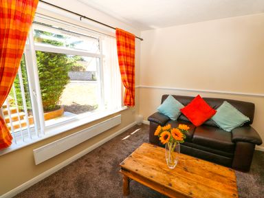 A living room with a brown leather sofa with three cushions and a wooden coffee table with sunflowers in a vase at Howards Hill West in Cromer