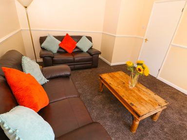A living room with brown leather sofas cushions on a wooden coffee table and flowers at Howards Hill West in Cromer