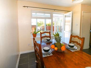 A dining area with a wooden table set with bowls and plates overlooking a garden at Howards Hill West in Cromer