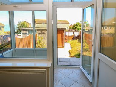 A tiled conservatory with white framed glass doors and windows looking out to a fenced backyard with grass and a wooden shed at Howards Hill West in Cromer