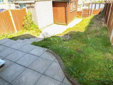 A backyard with a paved patio area grassy slope and wooden shed at Howards Hill West in Cromer