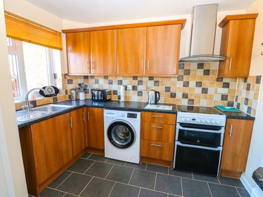 A kitchen with wooden cabinets a washing machine a stove a toaster and a kettle at Howards Hill West in Cromer