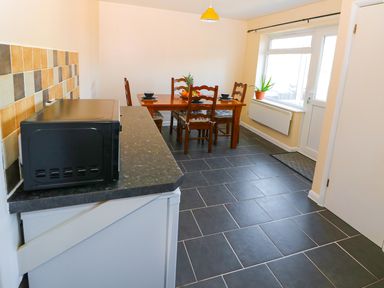 A kitchen with a black microwave on counter a wooden dining table with chairs and a window at Howards Hill West in Cromer