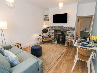 A living room with a sofa, armchair, ottoman, rug, fireplace, TV, and a small dining table set at Llys Madoc in Porthmadog