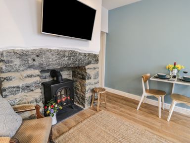 A sitting area with a stone fireplace wood stove and a dining table with two chairs at Llys Madoc in Porthmadog