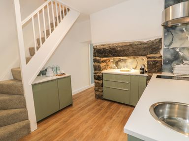 A kitchen with green cabinets a stone fireplace wooden floor and carpeted stairs at Llys Madoc in Porthmadog