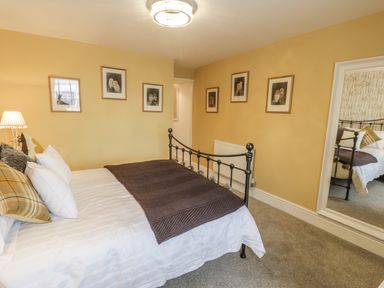 A bedroom with a metal bed frame white bedding and pillows a brown blanket on the bed framed pictures on yellow walls and a large wall mirror at Llys Madoc in Porthmadog