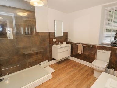 A bathroom with a shower, wall-mounted sink with mirror, toilet, towel rack, and window with blinds at Llys Madoc in Porthmadog