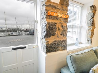 A corner of a room with a door open to a marina outside a stone wall with hooks a window and a blue sofa at Llys Madoc in Porthmadog