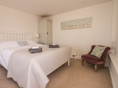 A bedroom with a white bed a wardrobe a lamp a chair with a cushion and a painting on the wall at Searles in Lympstone