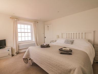 A bedroom with a large bed bedside tables a window with curtains and a television at Searles in Lympstone