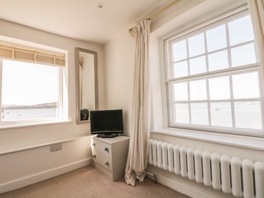 A corner of a room with two windows showing a view of water boats and hills a small chest of drawers with a television and a wall mirror at Searles in Lympstone
