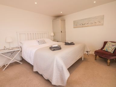 A bedroom with a bed with white and beige bedding two folded towels on the bed a chair with a pillow a wardrobe and bedside tables with lamps at Searles in Lympstone