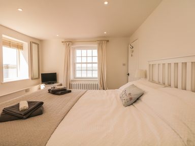 A bedroom with a bed a window with curtains a small television and folded towels at Searles in Lympstone