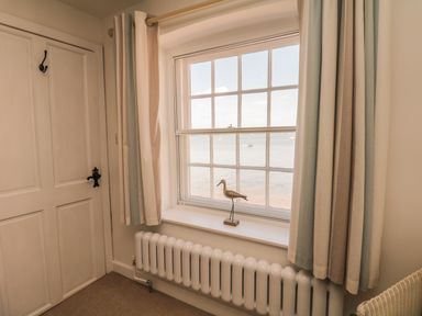A window with light curtains and a bird decoration on the sill above a radiator and a closed door to the left at Searles in Lympstone