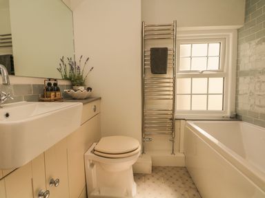 A bathroom with a sink toilet towel rack bathtub and window at Searles in Lympstone