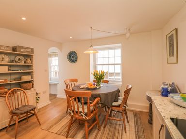 A dining room with wooden chairs around a round table with a gray tablecloth and a vase of flowers at Searles in Lympstone