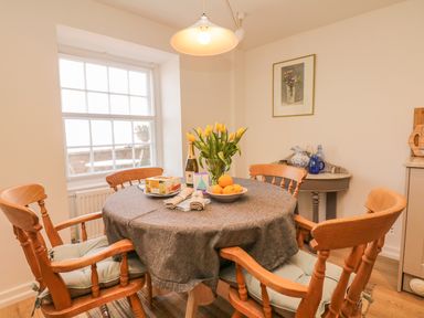 A dining area with a round table covered with a cloth and wooden chairs near a window at Searles in Lympstone