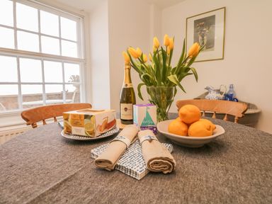 A dining table with a vase of yellow tulips a bottle of prosecco lemons in a bowl and a lemon drizzle cake at Searles in Lympstone