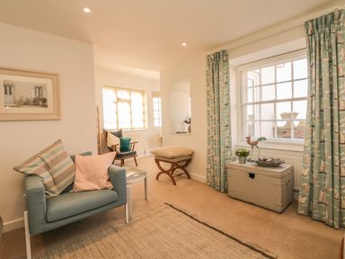 A sitting room with armchair cushions a wooden chair window curtains and a chest at Searles in Lympstone