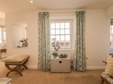 A room with a window with turquoise curtains a wooden bench with cushions and a painted chest with decorations at Searles in Lympstone