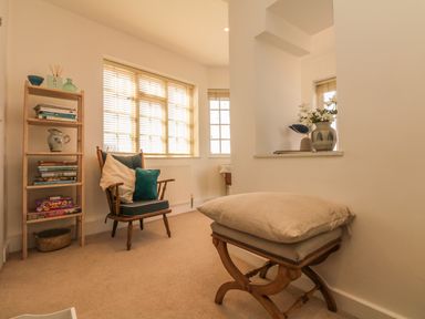 A sitting area with wooden chair and cushions next to a bookshelf with books and decor at Searles in Lympstone