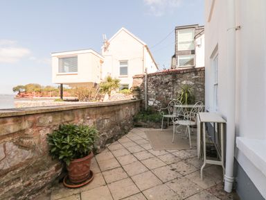 An outdoor patio with a stone wall two potted plants a white metal table and chairs and a folding table at Searles in Lympstone